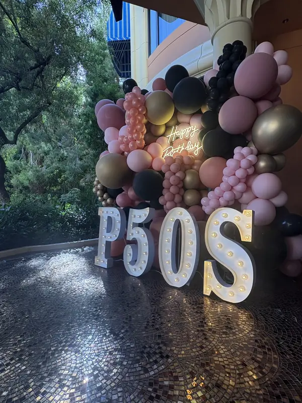Pink, black and gold balloon wall with a neon Happy Birthday sign and marquee letters