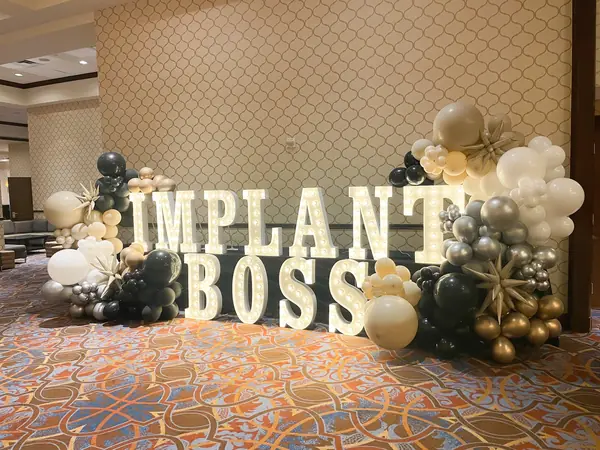 Marquee letters framed by black, gold and ivory balloons in a hotel ballroom foyer