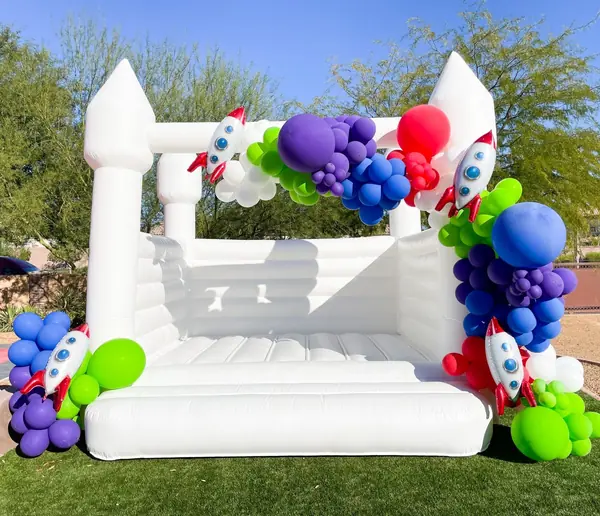 White bounce house trimmed with a bright rocket-ship balloon garland